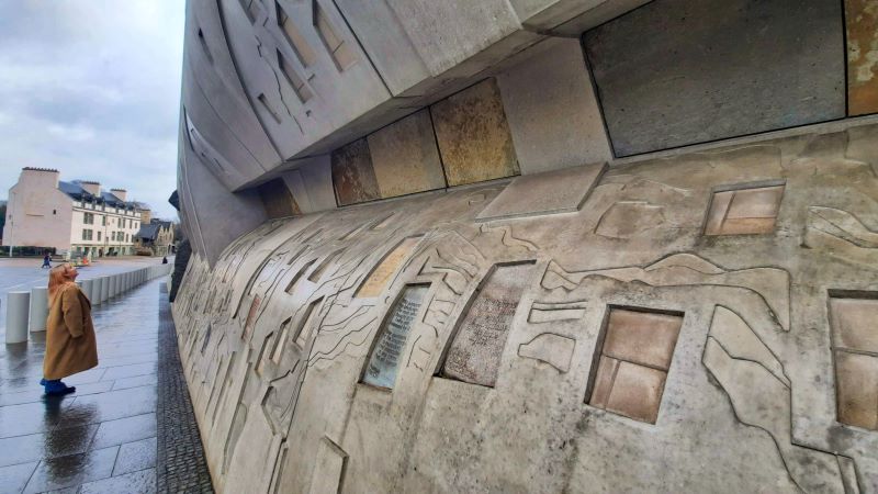 A person stands reading a quote carved into the Canongate Wall on the Royal Mile