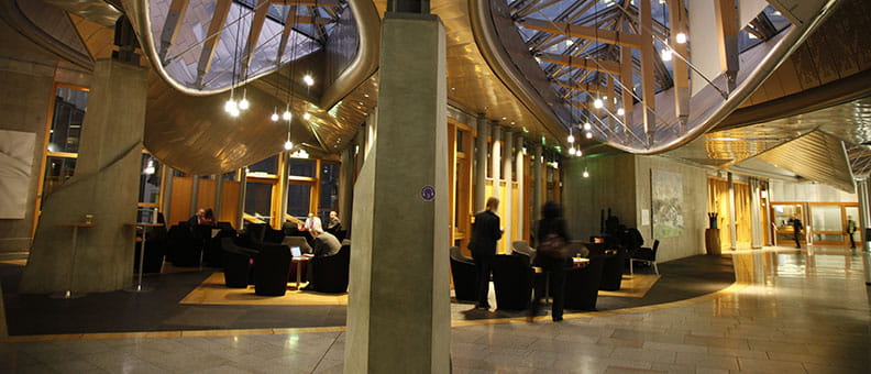 The Garden Lobby in the Scottish Parliament. It's evening and the lights are on. Members of staff are chatting around the room.