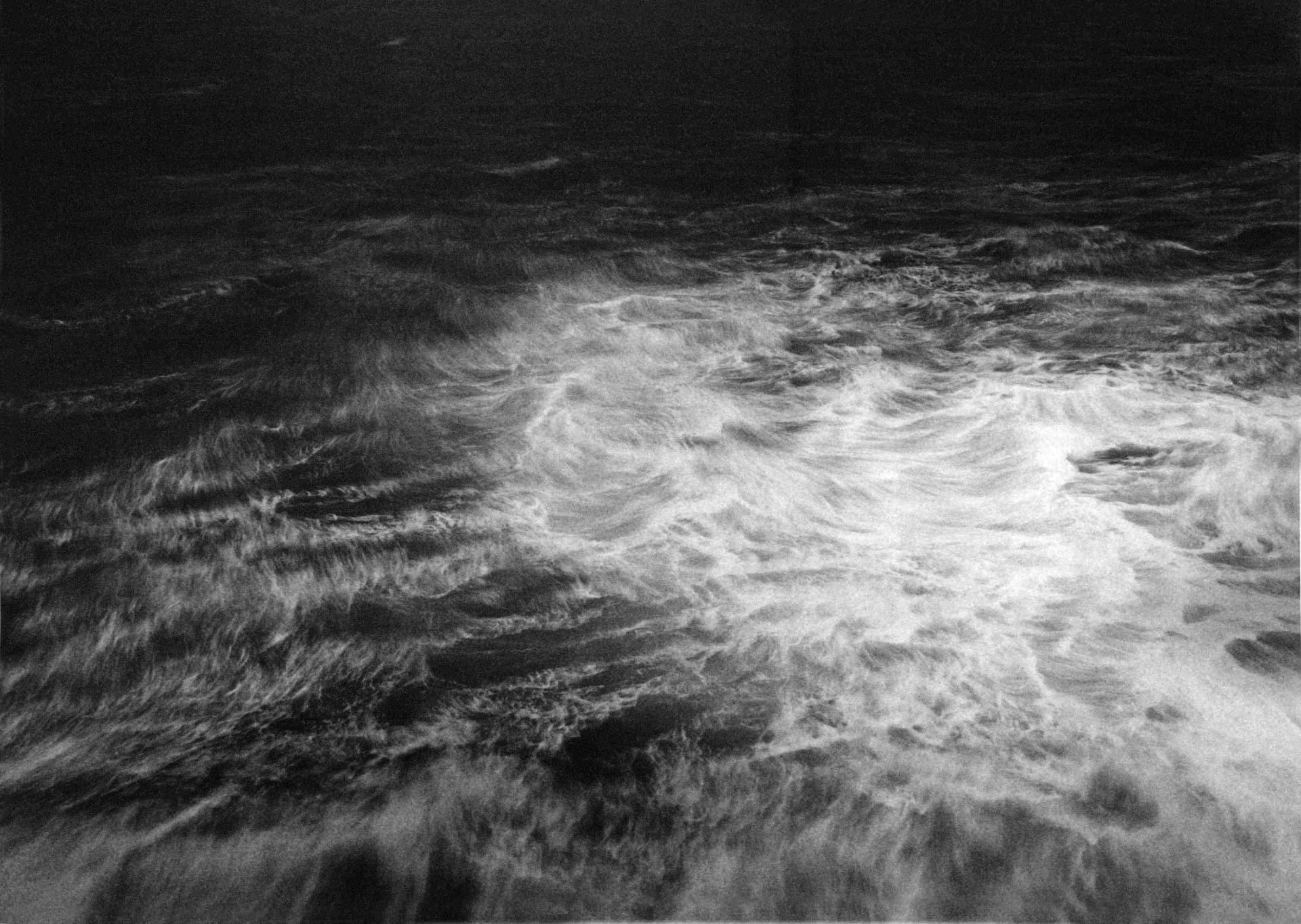 Large black and white photograph of the sea, with no sky. 