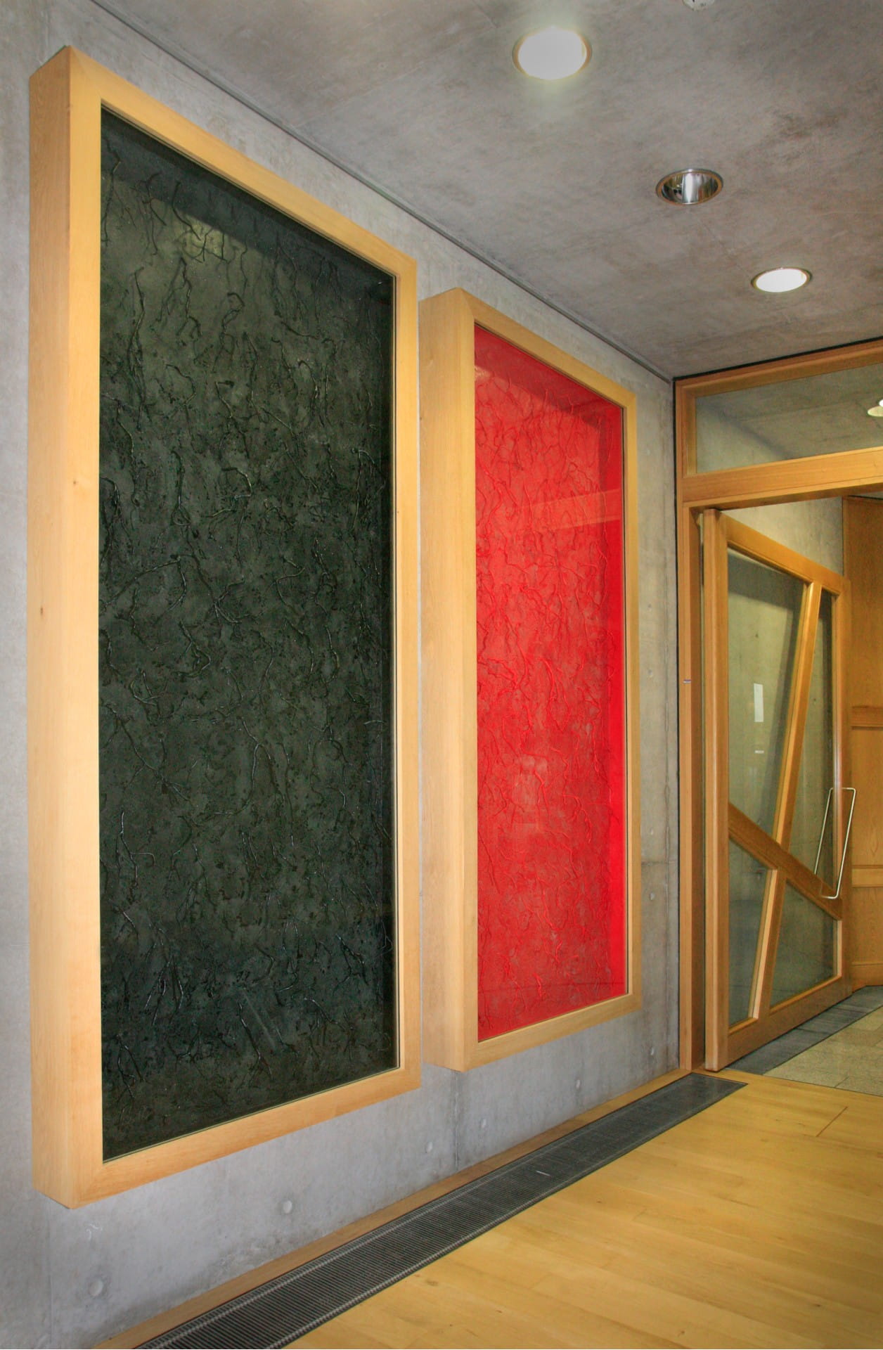 Two large glass cases, from ceiling to floor. Inside both are lots of heather twigs encased in wax and with a dusting of salt. One case has twigs in red wax, the other black. 