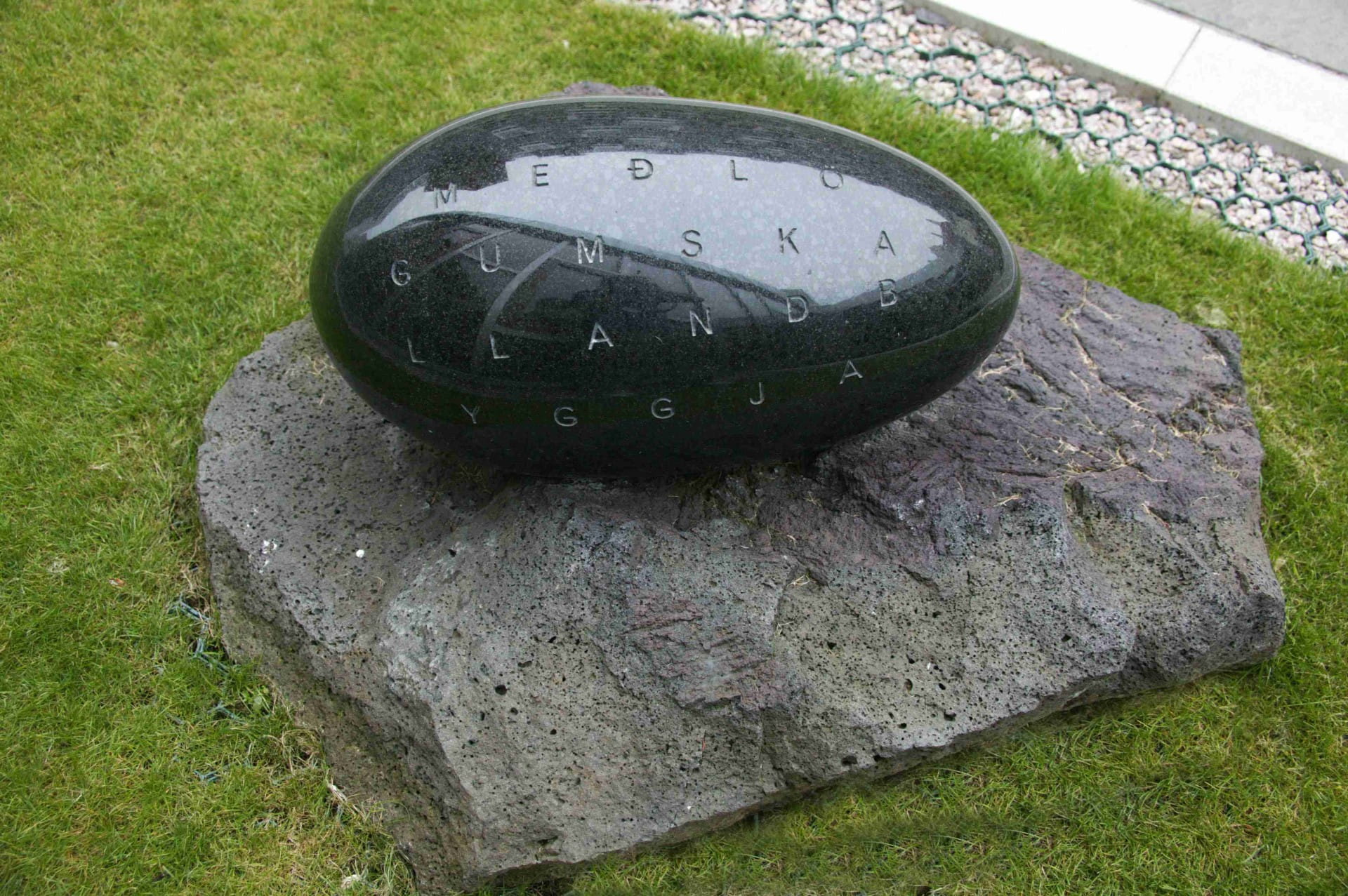 Polished and carved black granite egg on a ground level plinth of volcanic rock. 